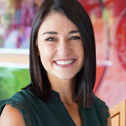 A woman named Alexa Consul smiling brightly in front of a abstract art painting.