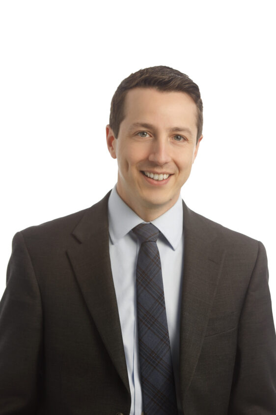 A man named Dan Salamone smiling in a black suit, blue patterned tie and light blue button down.