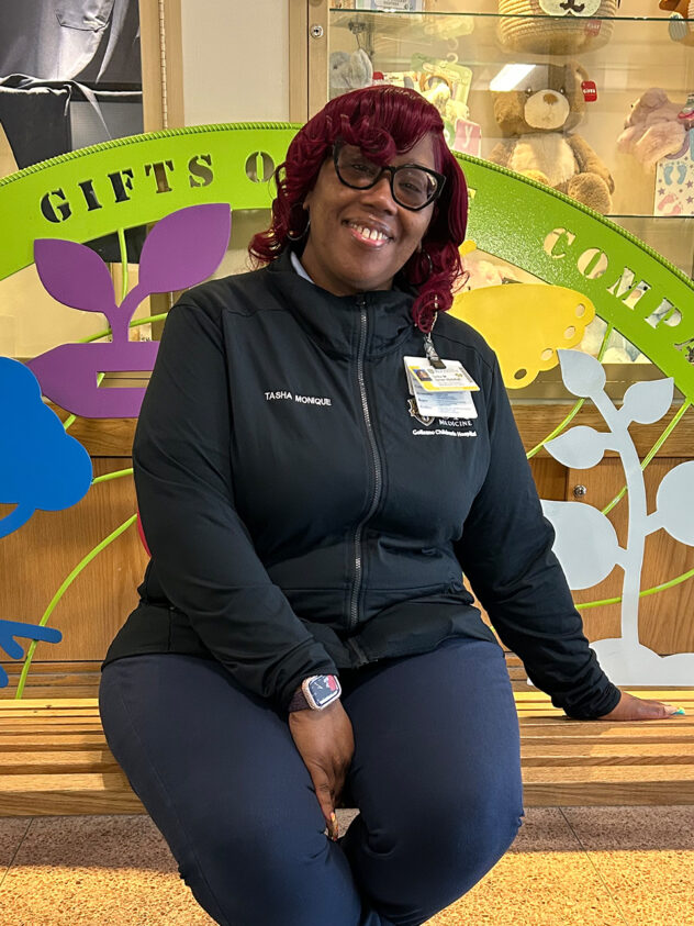 A woman named Tasha Turner is sitting on a bench with a metal back made of different shapes and colors: blue tree, yellow butterfly, and gray sprout.