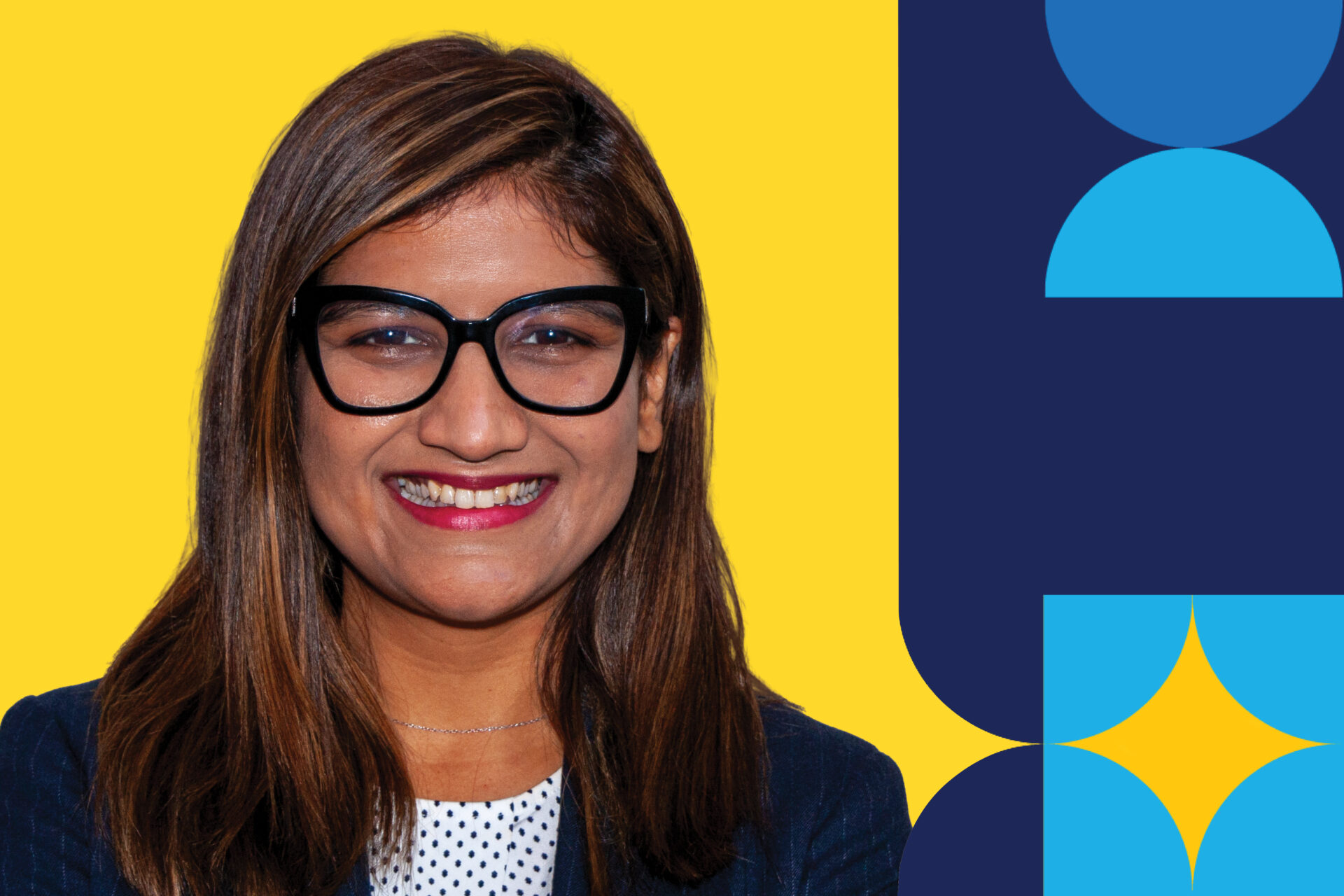 A woman named Radhika Thakkar smiling brightly wearing glasses and a black blazer in front of a yellow background.