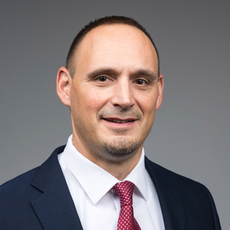 A man named Alan McNiff in a white button down, red tie, and black blazer.