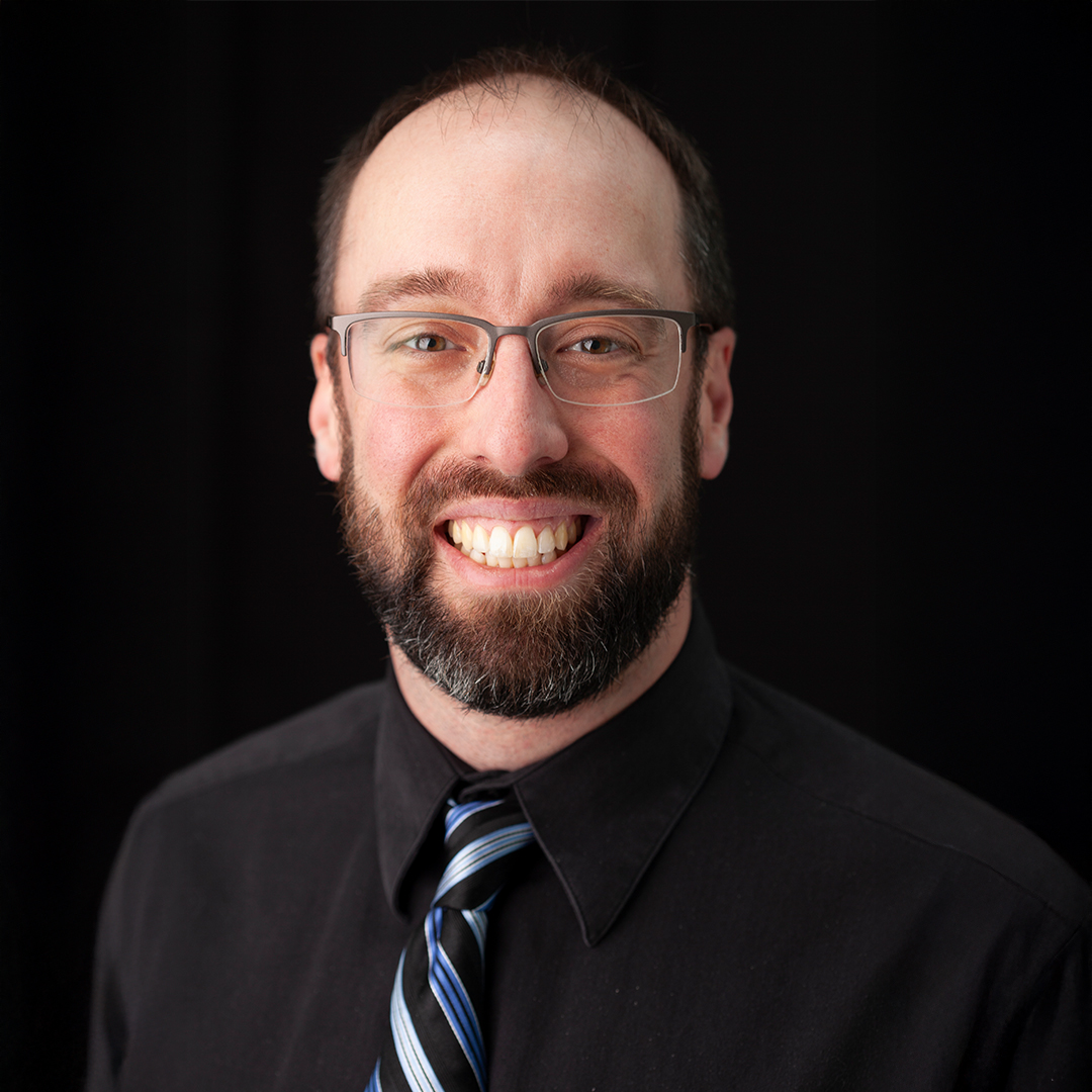 A man named Andrew Gudonis smiling brightly in a black button-down down, bust up.