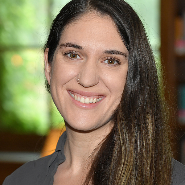 A woman named Ashlee Huff is smiling brightly in front of a window with her hair parted to the right.