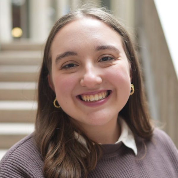 A woman named Madison Esposito is smiling brightly in front of a flight of stairs.