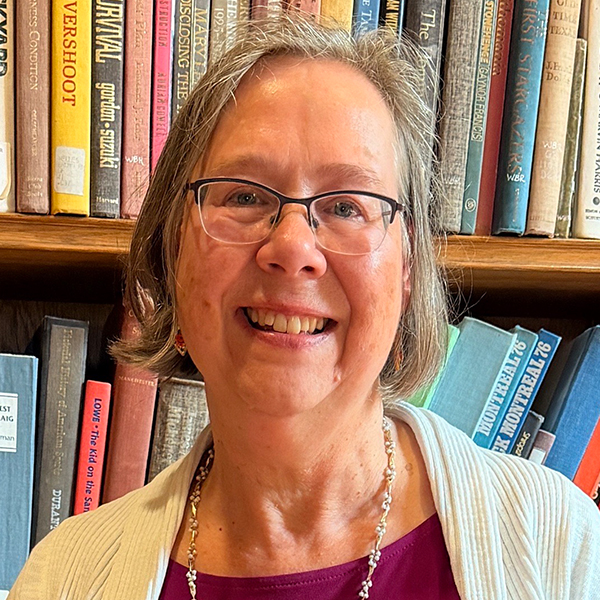 A woman named Sue Cardinal smiling brightly in front of a shelf of books.