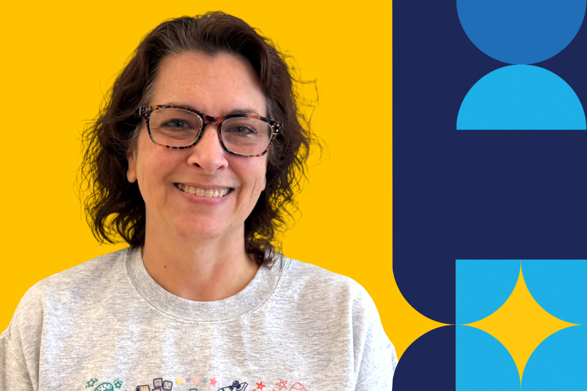 A woman named Jennifer Notali is smiling brightly with a gray sweater and glasses on in front of a yellow background.