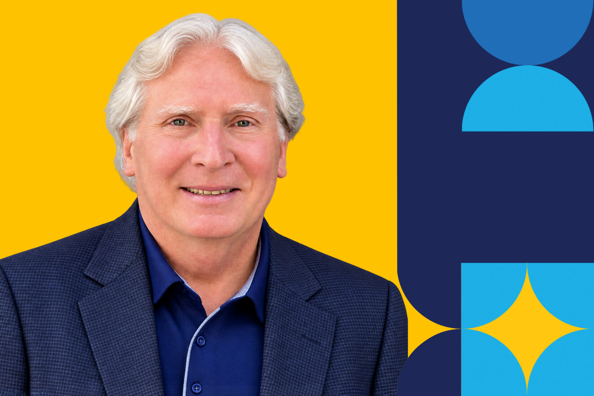A man named Robert Wagnewr smiles in a navy blue jacket in front of a yellow background from the shoulders up.