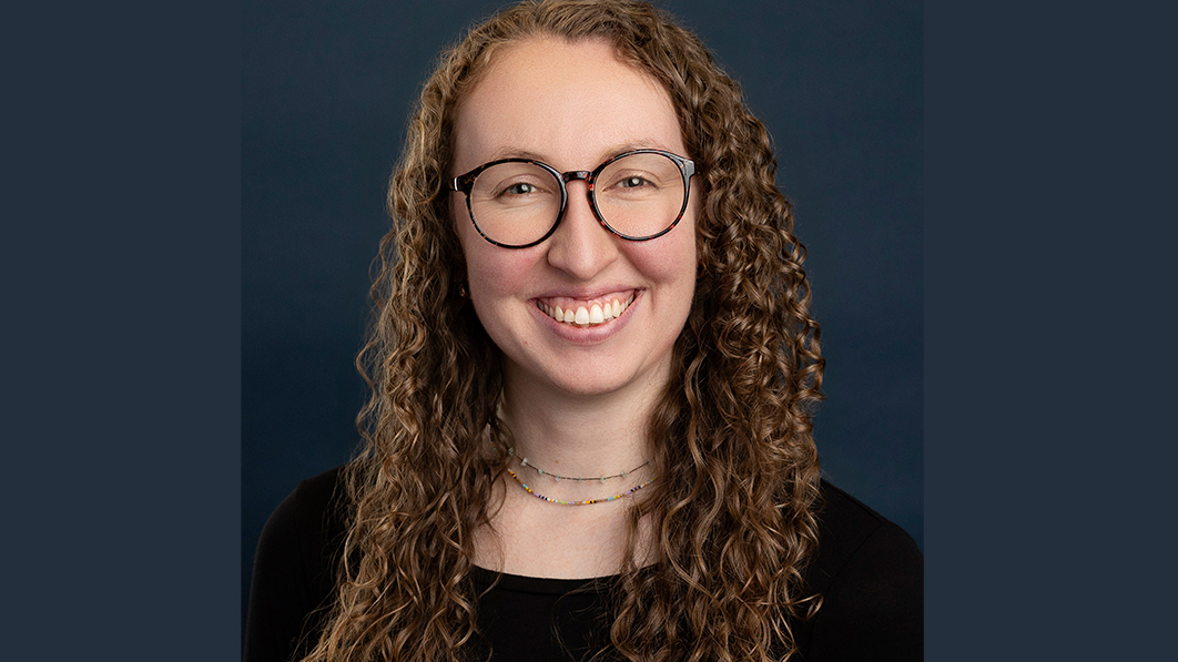 A woman named Makenzie Mathews is smiling brightly in a black shirt in front of a gray background.
