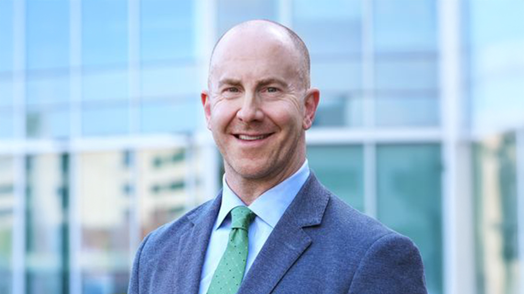 A man named Ryan Fields is smiling brightly in a blue suit, green tie, and light blue button down.