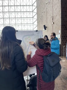 Two students map their travel routes with colored strings on a campus map displayed in Wilson Commons.