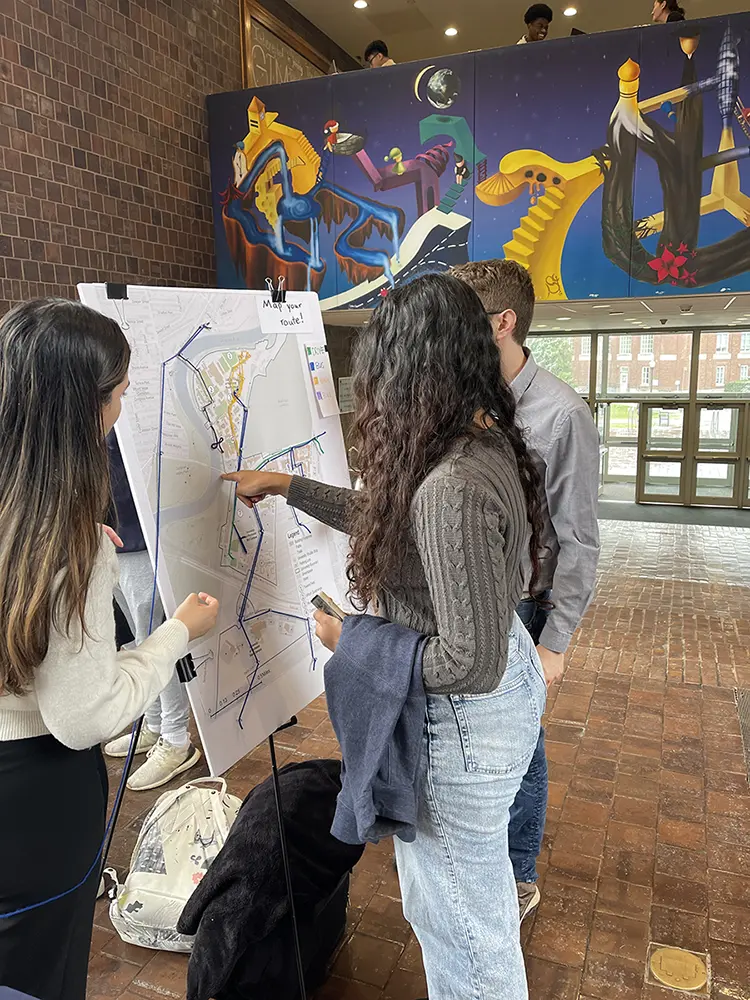 POINT AND MAP: Three students map their travel routes with colored strings on a campus map displayed in Wilson Commons.