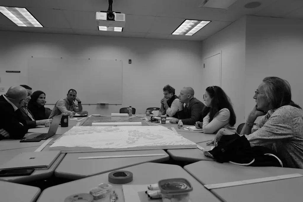 Members of the master planning Executive Committee meeting with design and architecture consultants, seated before a 3-D replica of University campuses.
