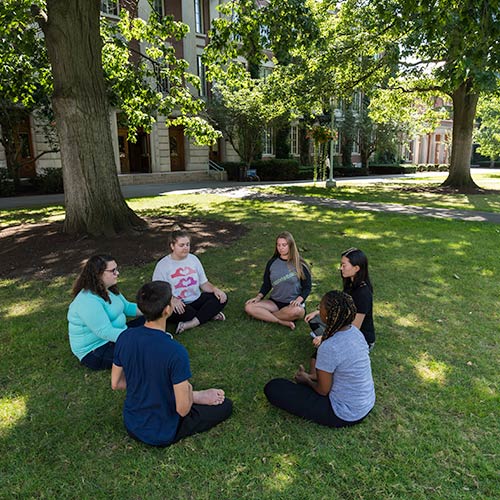 group of students medititating in a circle under a tree.