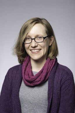 A professional headshot of an individual wearing glasses and a purple scarf.
