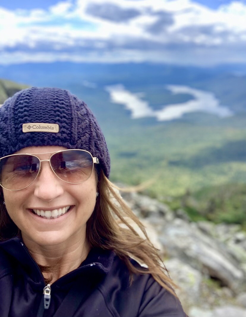 Picture of a female smiling on top of a mountain.