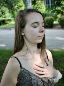 Picture of a female in front of Rush Rhees meditating with a hand over her heart. 