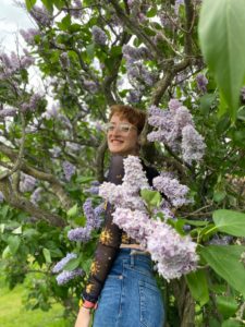 A graduate student smiling amongst lilacs at Highland Park. 