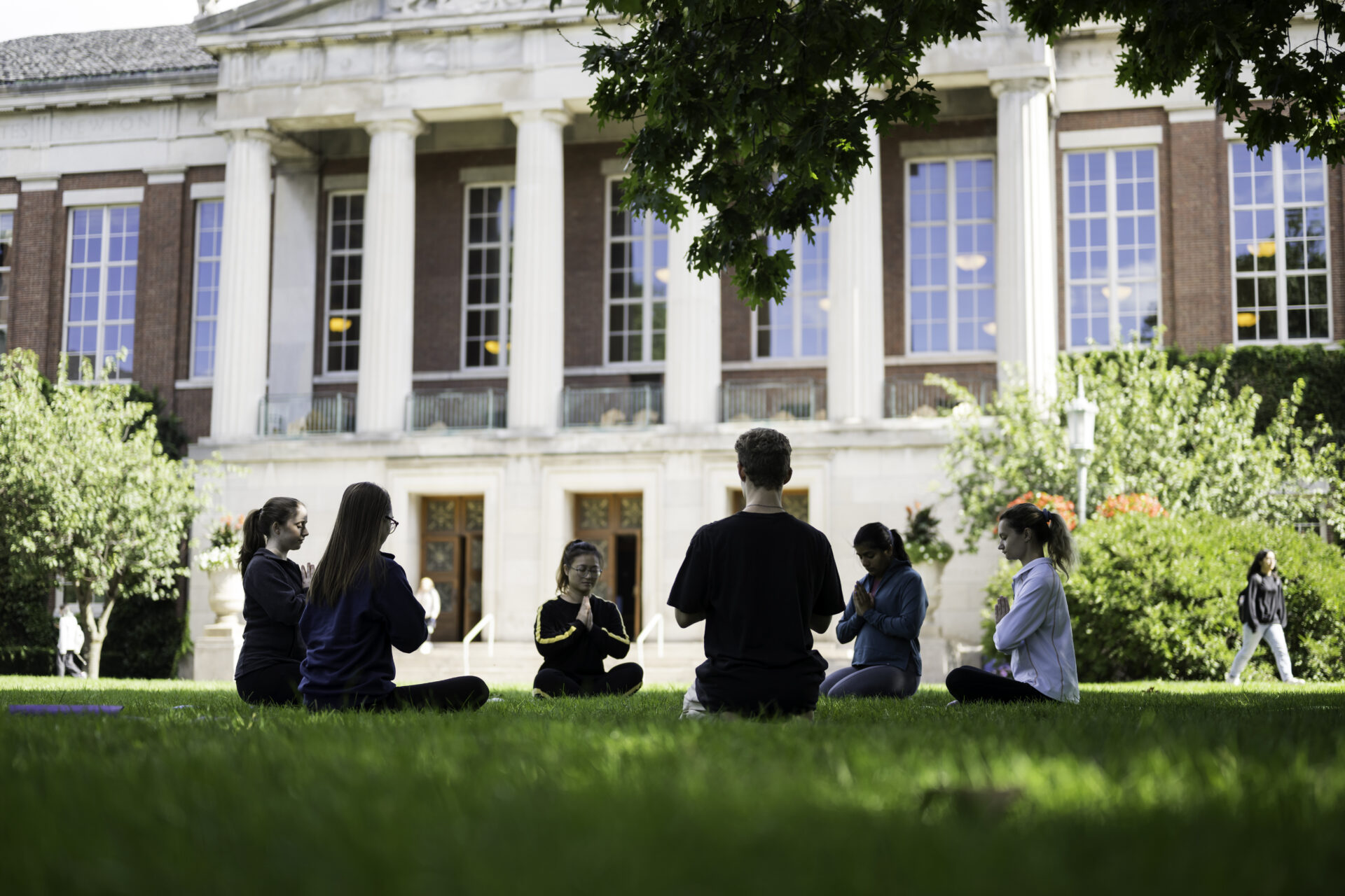 Students in meditation postures on the Eastman Quad in front of Rush Rhees