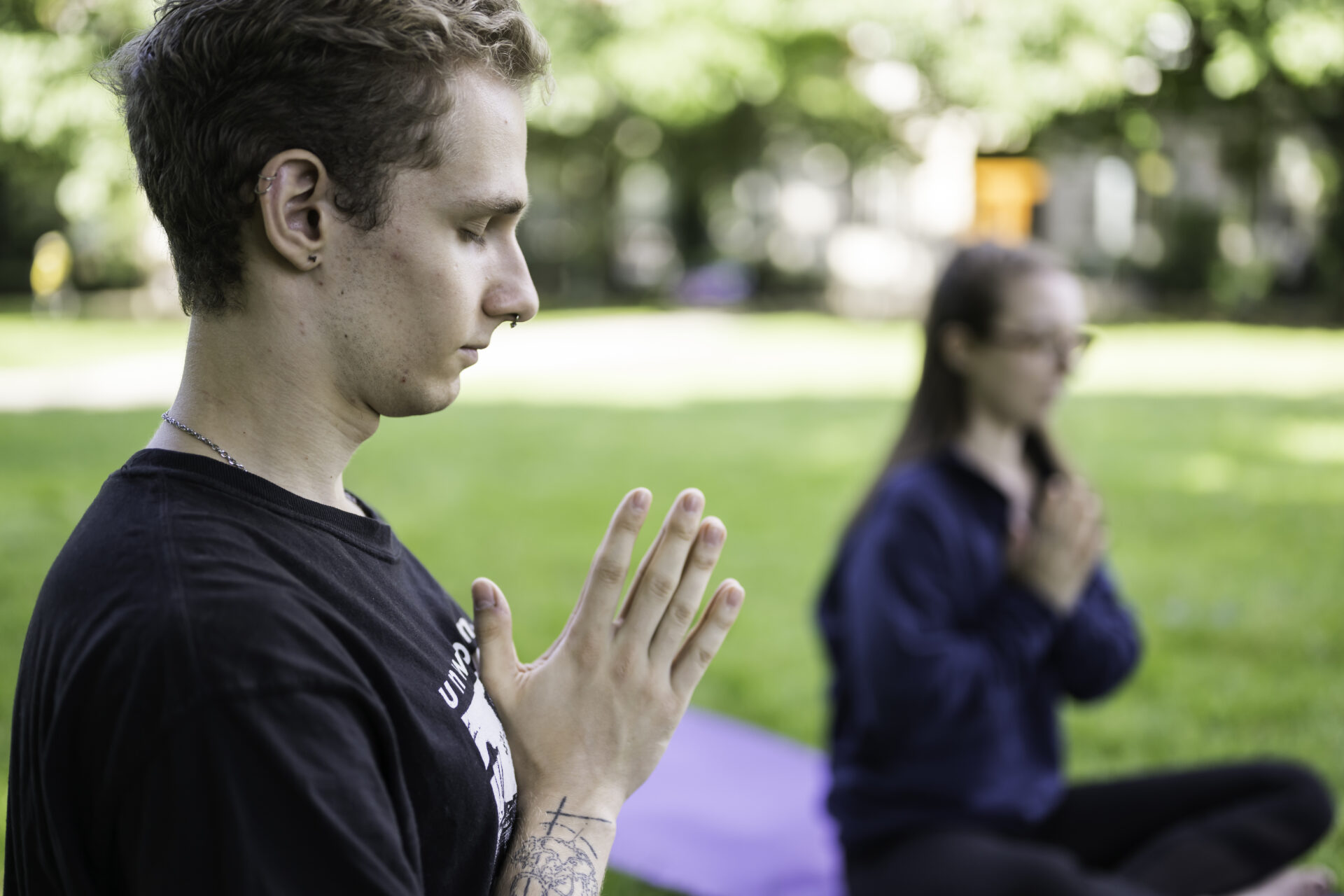 Adults with hands at heart center bowing heads with eyes closed in meditation postures outside
