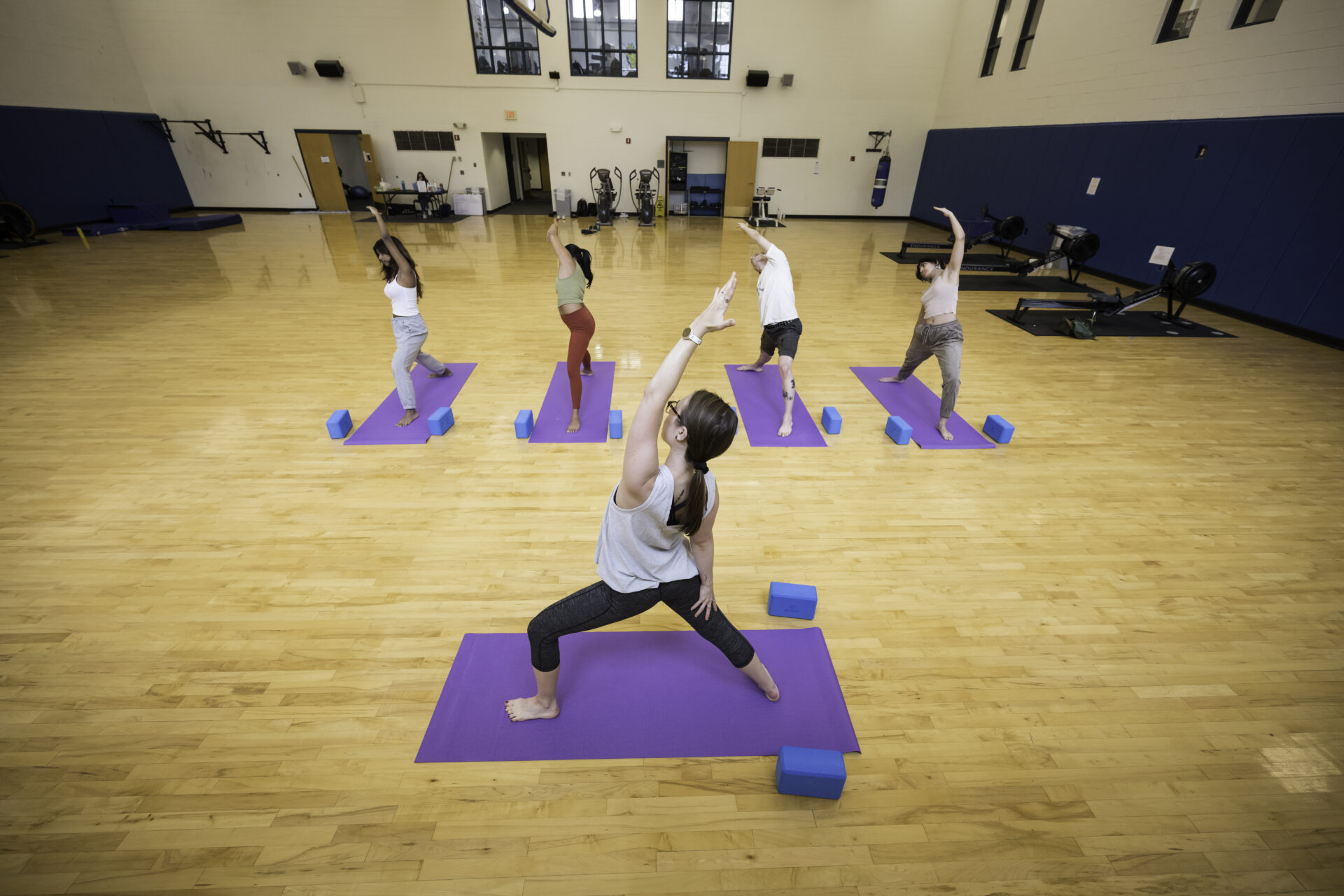 A woman leading a yoga class demonstrating peaceful warrior with four other people following.