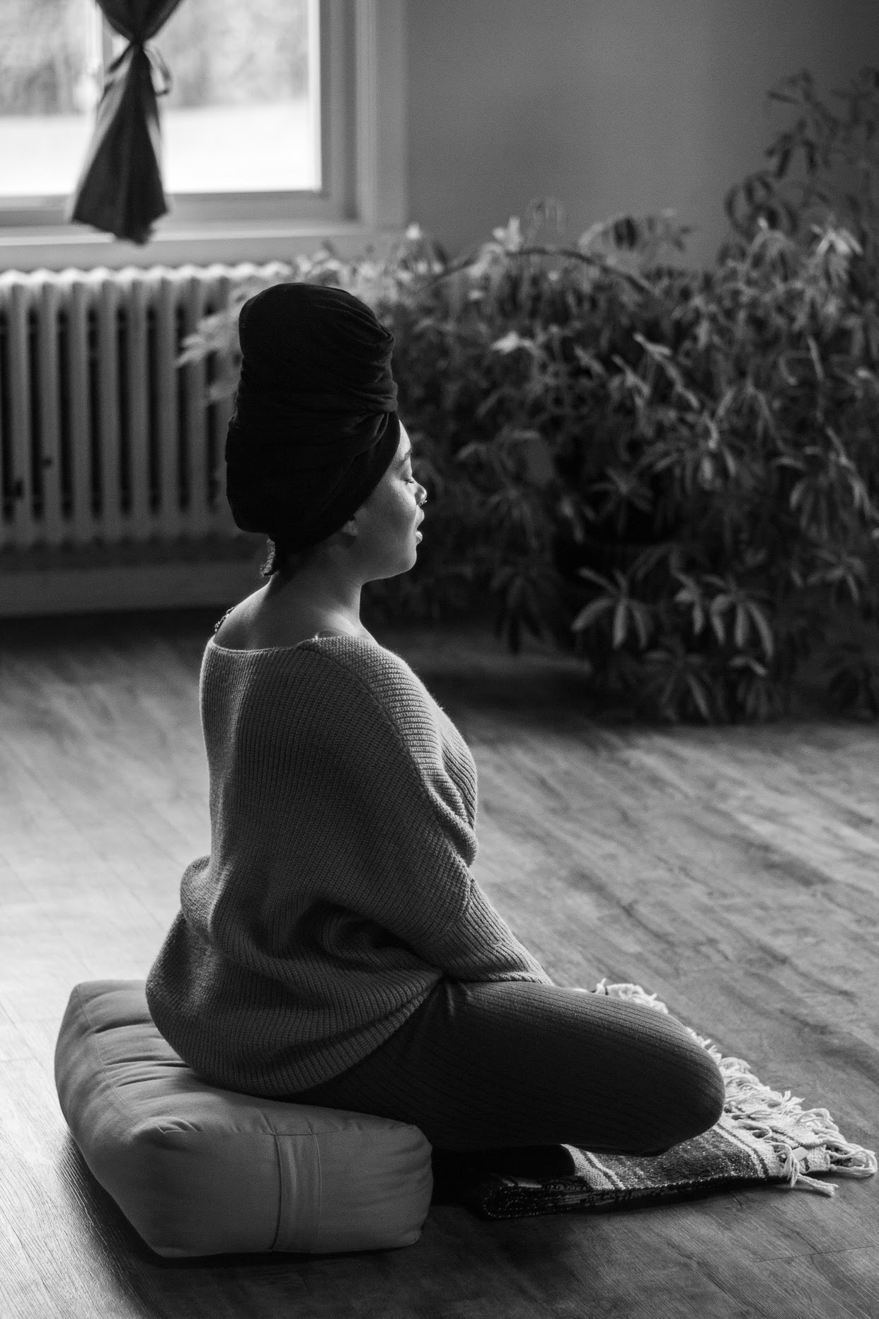 A black and white photo of a woman sitting on a yoga bolster in a meditation posture
