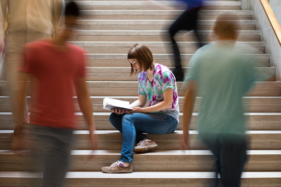 young woman reading a book on stairway, as others blur by
