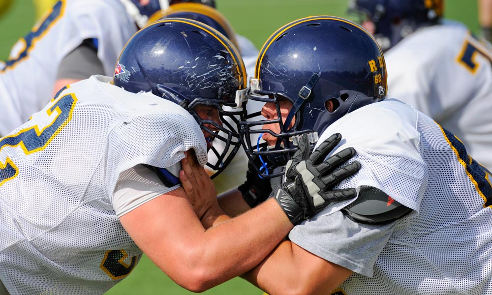 two football players butting helmets, helmets showing signs of wear