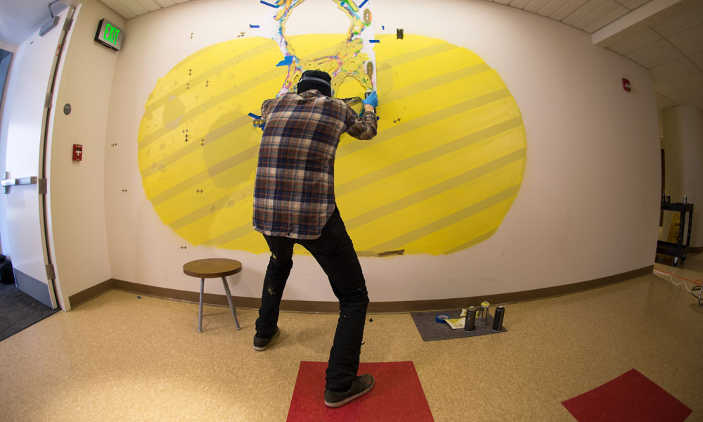 Feature image graffiti artists using yellow spray point to paint a mura on the wall of Rettner Hall