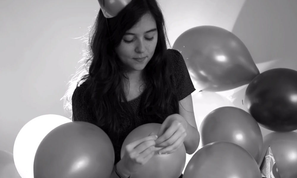 Feature image still image from a black-and-white film showing girl blowing up balloons