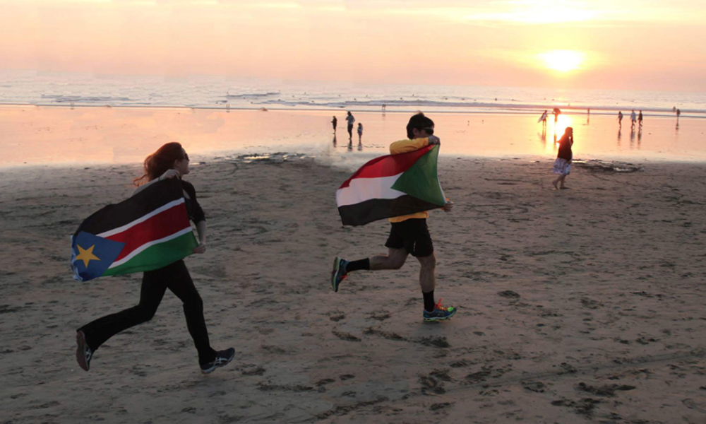 Feature image two people running across a beach with the flags of Sudan and South Sudan