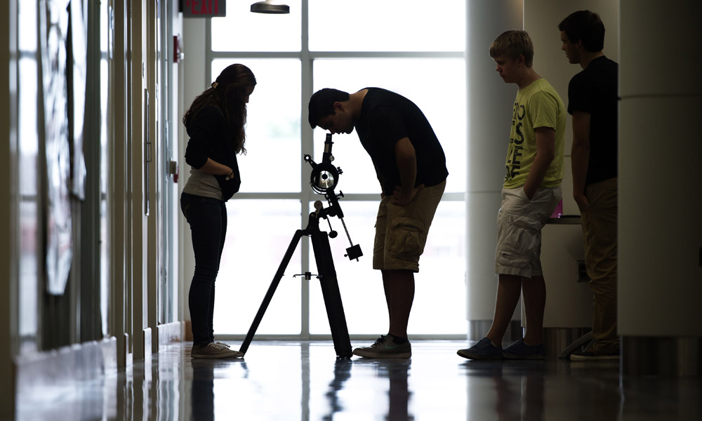 Feature image students in a backlit hallway, one of them looking into a telescope