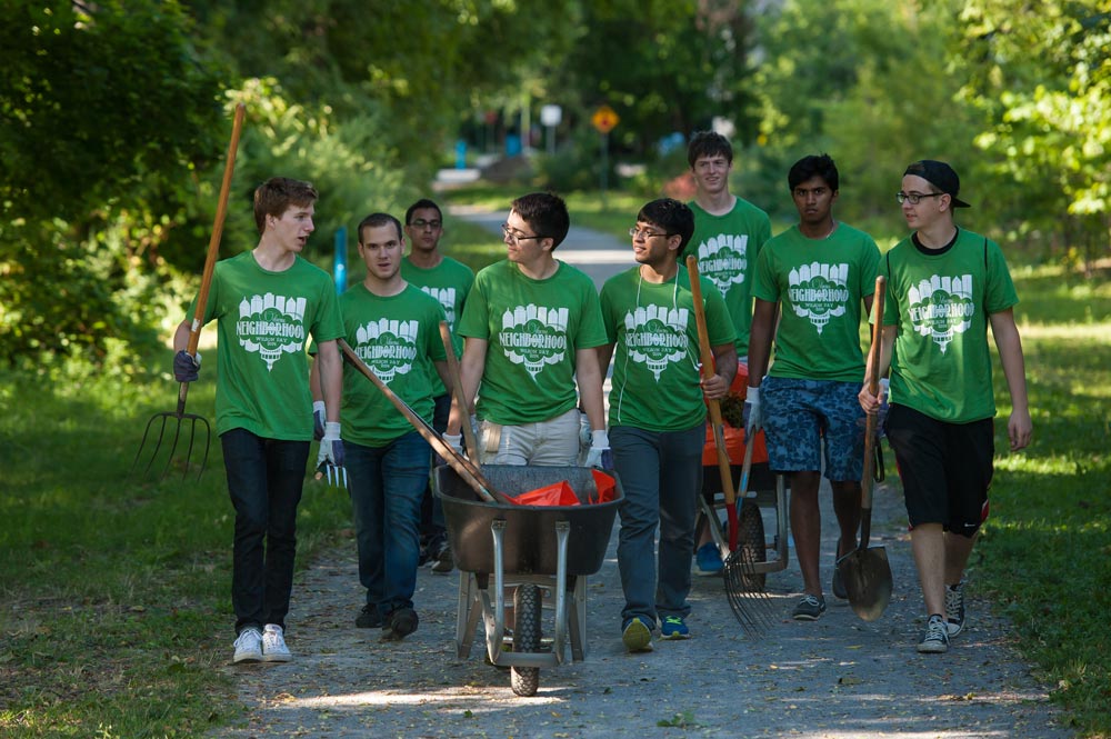 Feature image large group of students in matching t-shirts pushing wheelbarrows and carrying gardening equipment