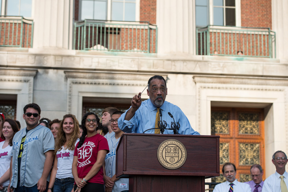 Feature image Paul Burgett behind the podium on stage at convocation with student musicians behind him