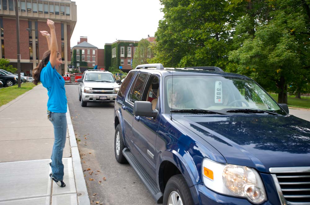 student raises her arms and cheers as a car pulls up in front of residence hall