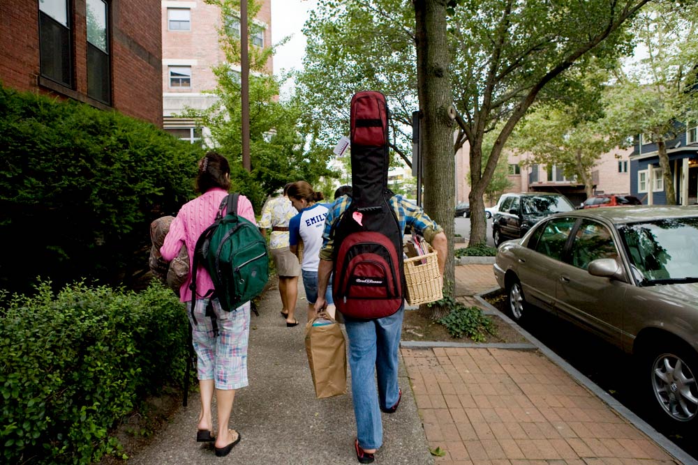 student walks along downtown street with a guitar case on his back.