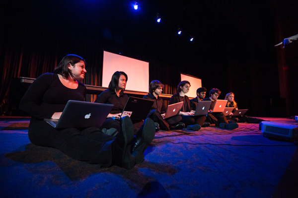 Feature image groups of students sitting on a stage holding laptops