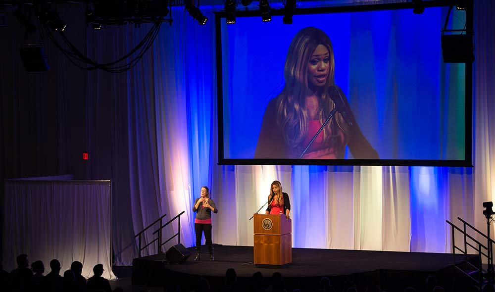 Feature image Laverne Cox on stage, with a giant screen projecting her image