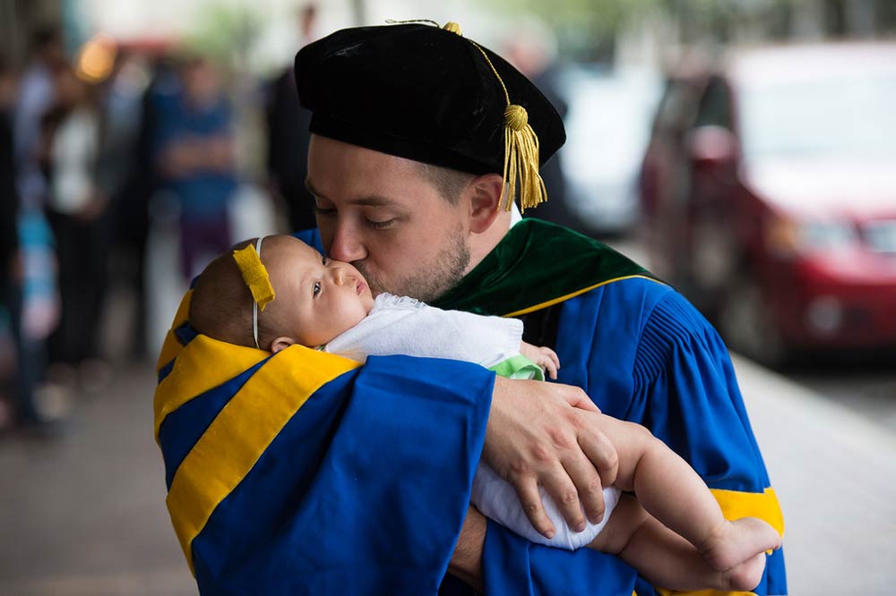 man in graduation cap and gown kissing a baby