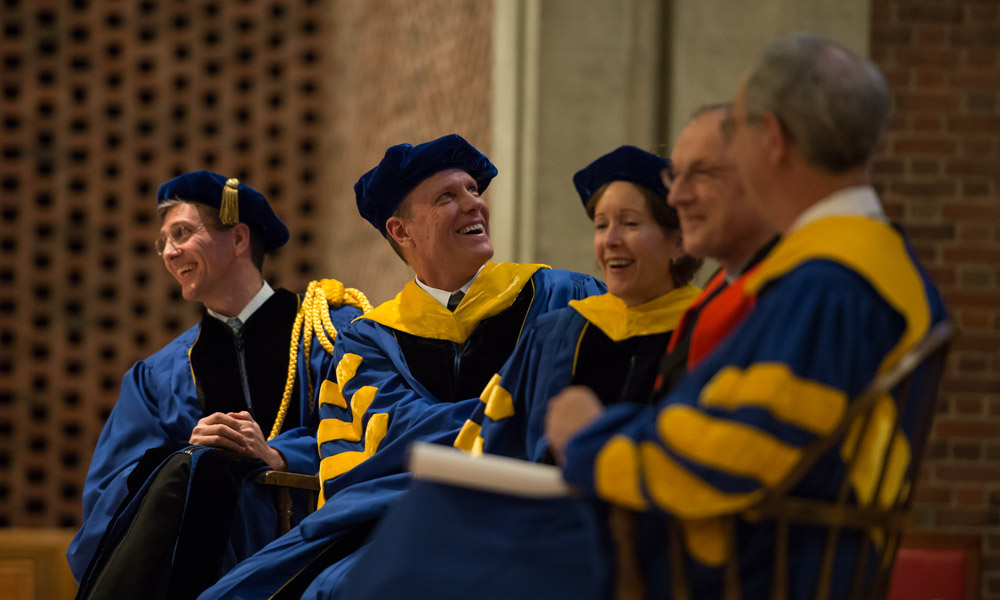 Feature image platform party in academic regalia looks over the shoulder at a screen, laughing
