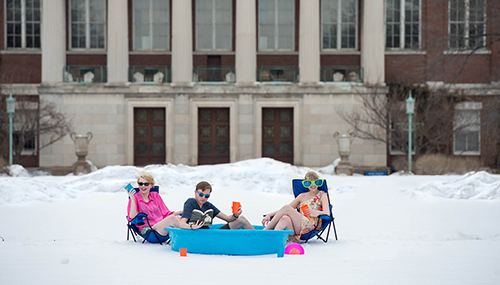 three students sitting in a pool on a snow-covered quad.