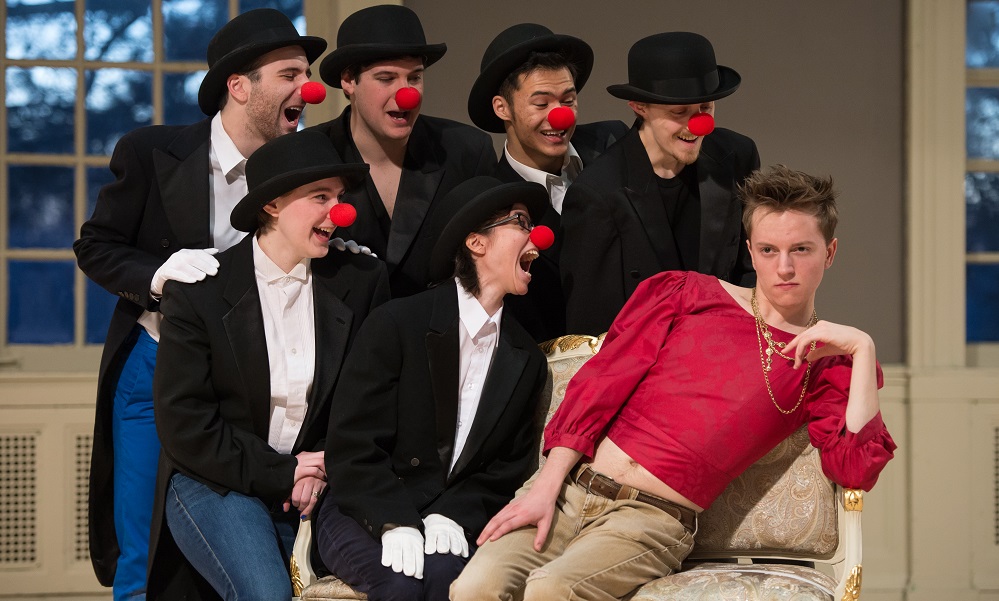Feature image actors sitting on a couch, all but one of them wearing bowler hats and clown noses