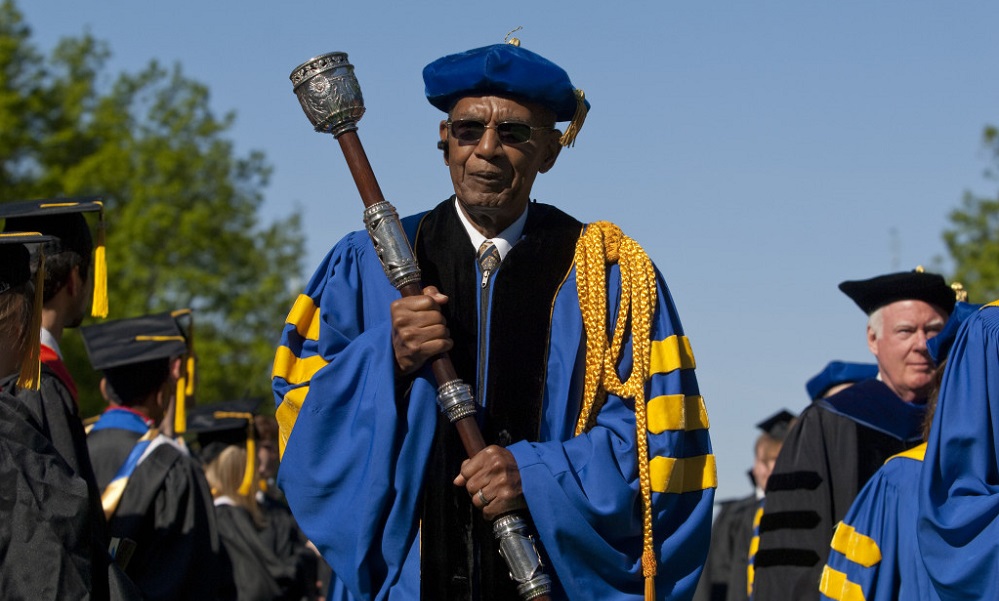 Feature image Jesse Moore in academic regalia carries the mace at the head of a commencement procession