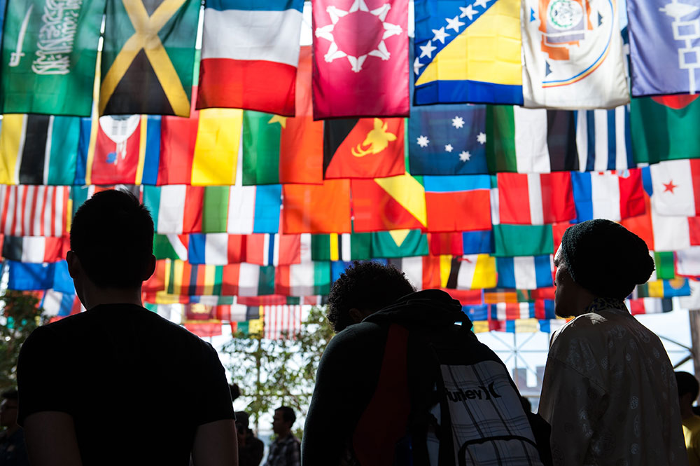 Feature image group of students stand solemnly under large grouping of flags