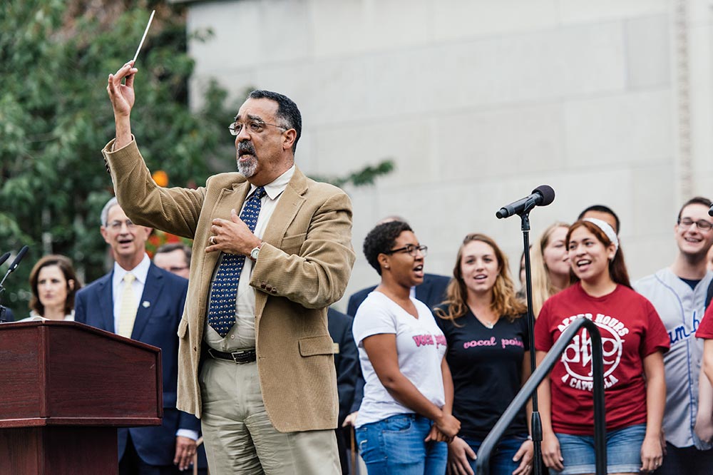 Feature image Paul Burgett conducting as student sing on stage