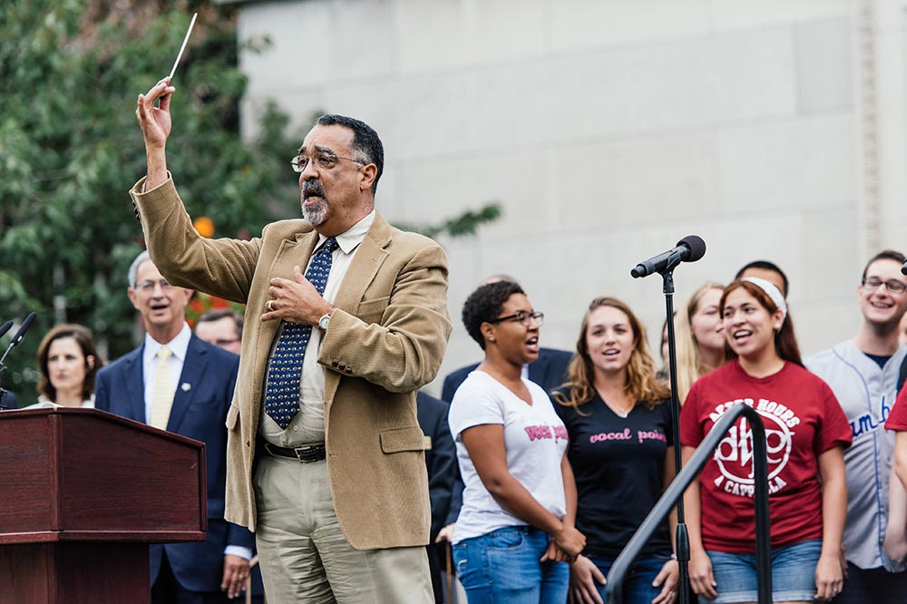 Paul Burgett conducting as student sing on stage