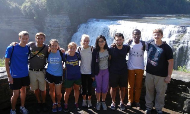 group of students pose before water fall