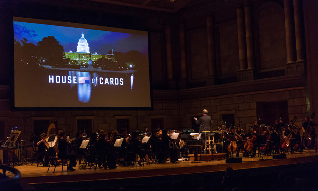 Jeff Beal conducting on stage with large House of Cards title on screen above musicians