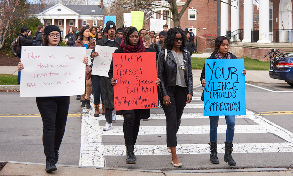 Feature image student protester march with signs that read YOUR SILENCE UPHOLDS OPRESSION