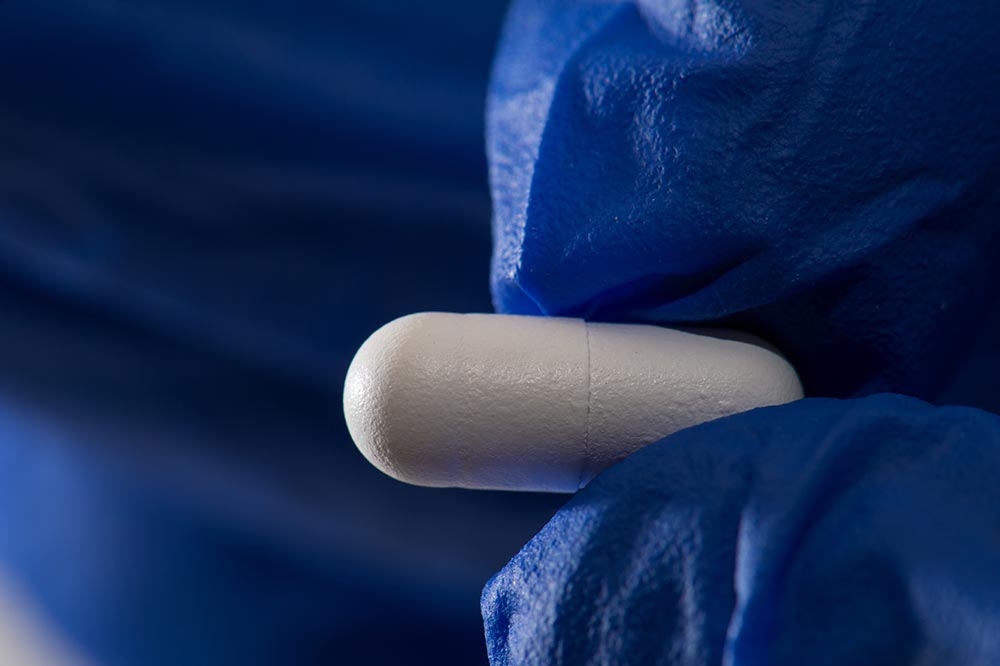 gloved hands holding a pill