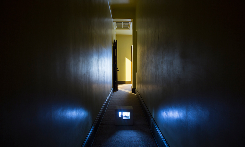 Feature image art exhibit shows a blue glowing box in a darkened hallway